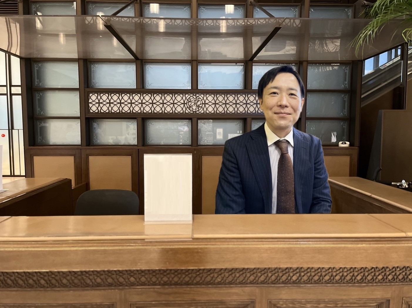 スーツを着た男性が木製のデスクの後ろに立っている旅館のフロントの様子