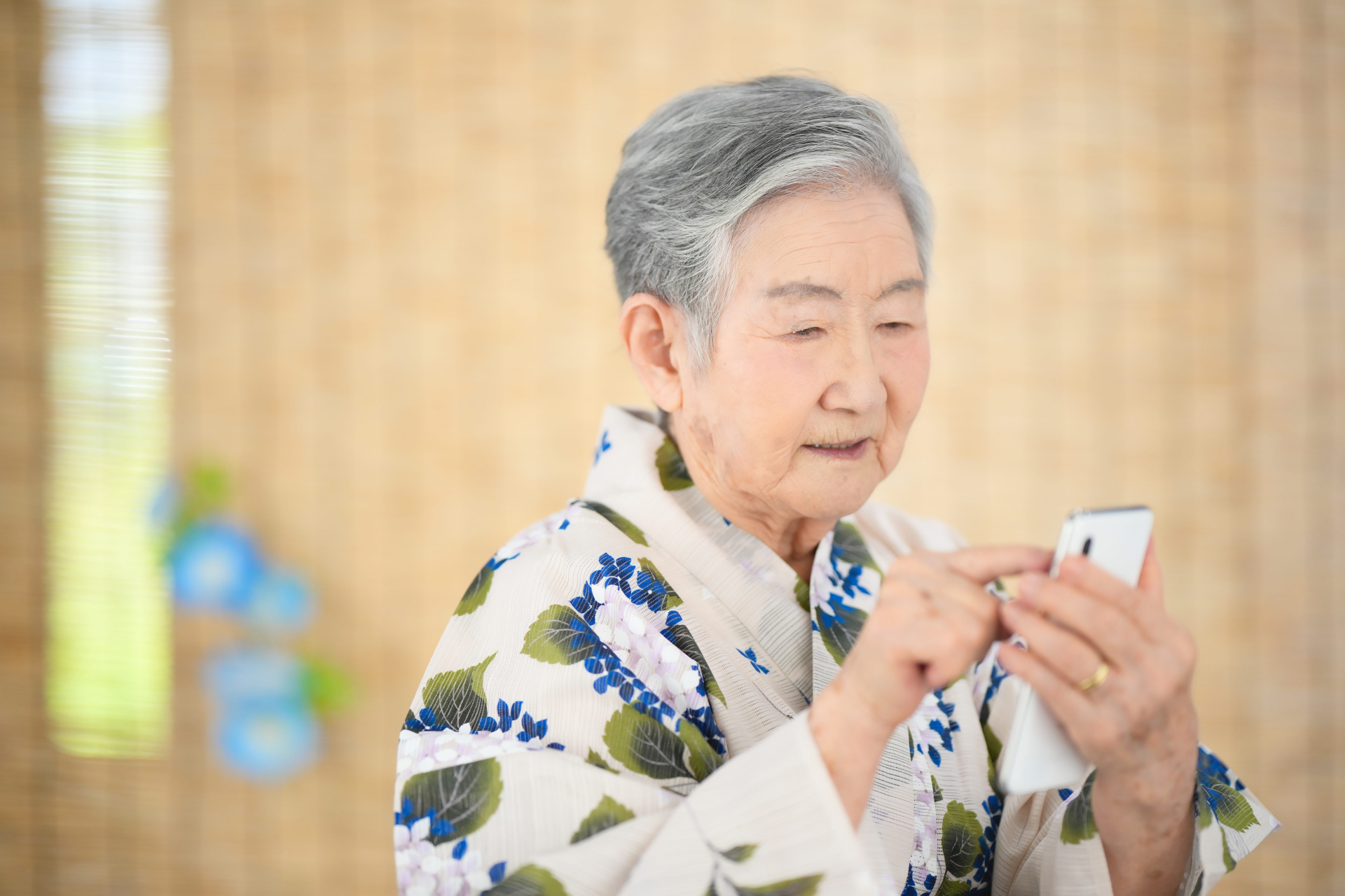 着物を着た年配の女性がスマートフォンを使っている様子を描写した画像です。