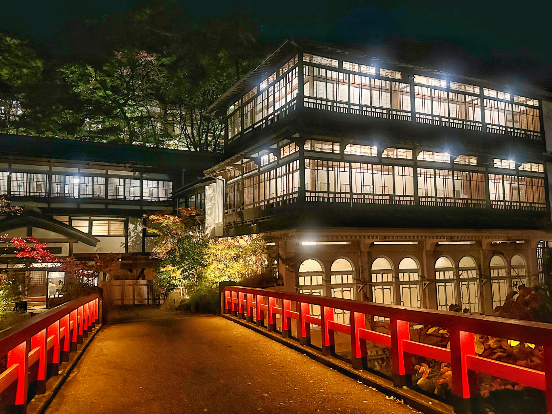 夜の静けさの中、赤い橋が旅館へと続く様子を捉えた画像です。